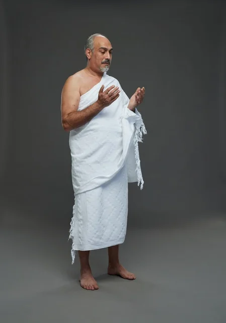 Saudi Man in Ihram Praying Against Grey Background