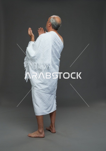 رجل سعودي بملابس الإحرام يدعو بخلفية رمادية