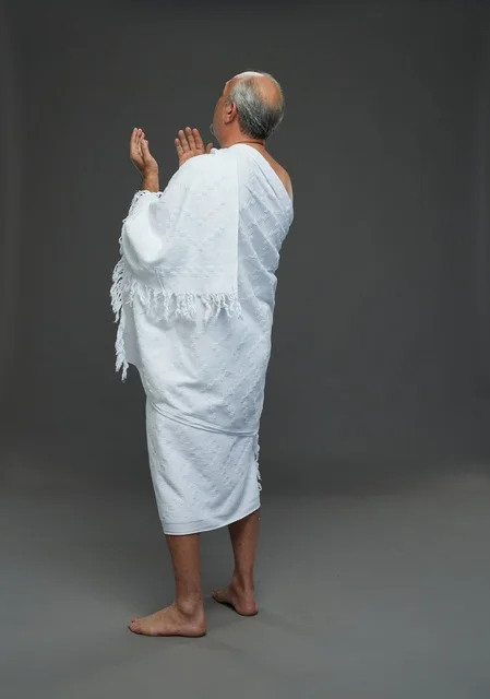 رجل سعودي بملابس الإحرام يدعو بخلفية رمادية