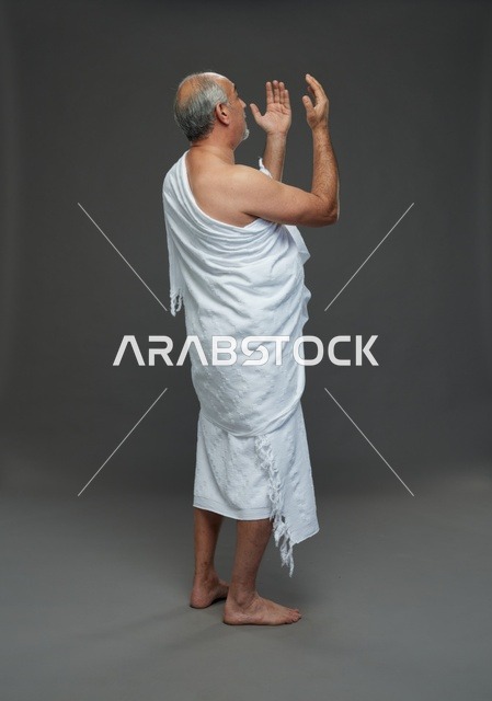 رجل سعودي بملابس الإحرام يدعو بخلفية رمادية