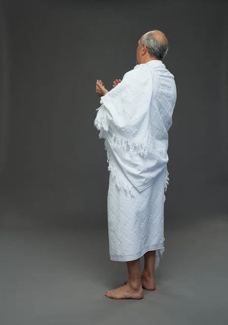 رجل سعودي بملابس الإحرام يدعو بخلفية رمادية