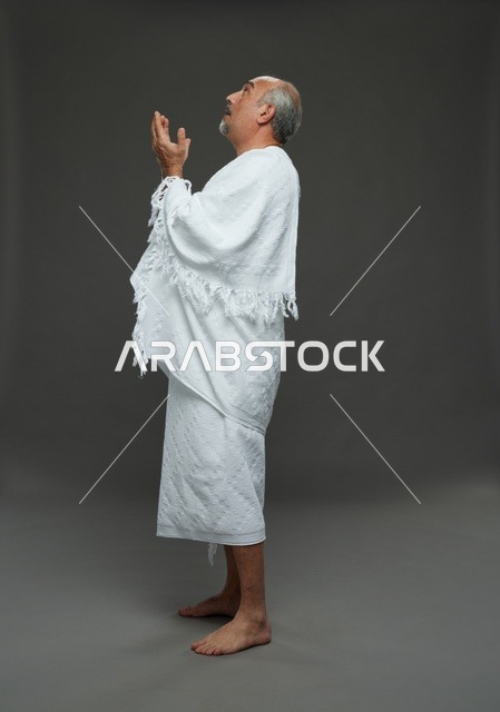 رجل سعودي بملابس الإحرام يدعو على خلفية رمادية
