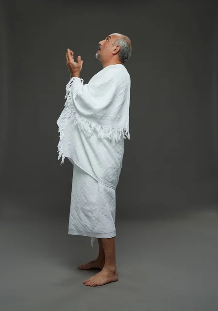 Saudi Man in Ihram Clothes Praying Against Grey Background