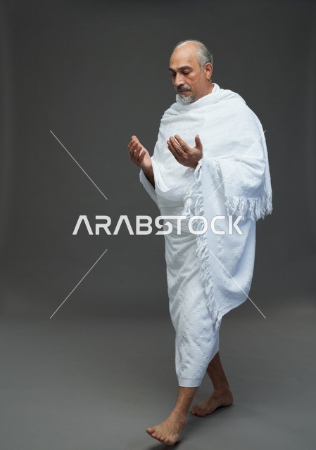 رجل سعودي بملابس الإحرام يدعو بخلفية رمادية
