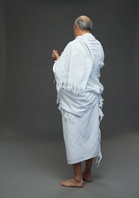 رجل سعودي يرتدي ملابس الإحرام ويدعو على خلفية رمادية