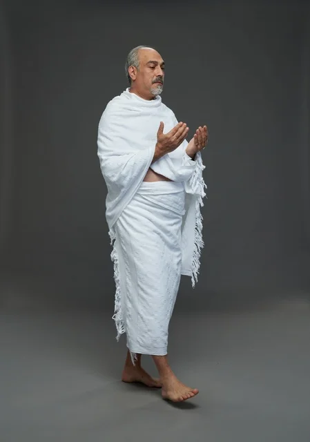 رجل سعودي بملابس الإحرام يدعو على خلفية رمادية