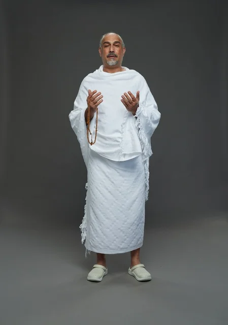 رجل سعودي بملابس الإحرام البيضاء يدعو بالسبحة في الاستوديو