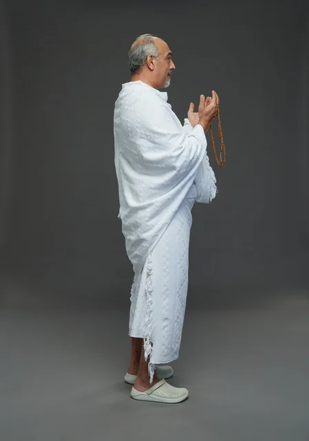 رجل سعودي بملابس الإحرام يدعو أمام خلفية رمادية