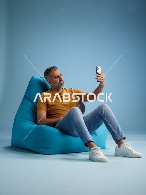 رجل سعودي متوسط العمر يلتقط صورة سيلفي على كرسي بين باق