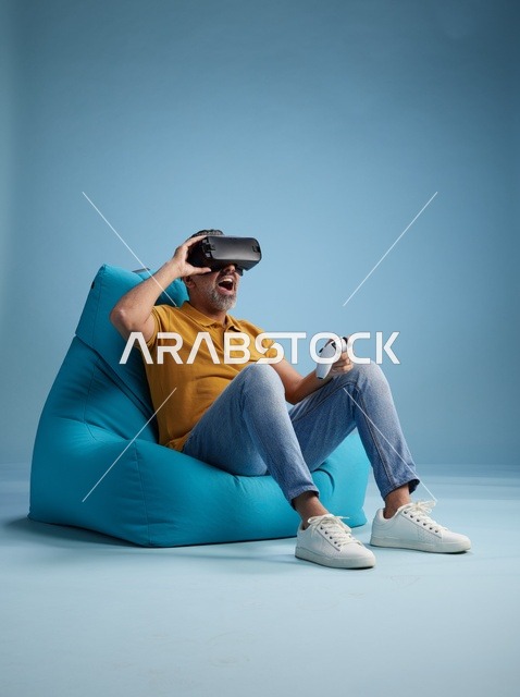 Saudi Man Playing VR Games on Bean Bag Blue Background