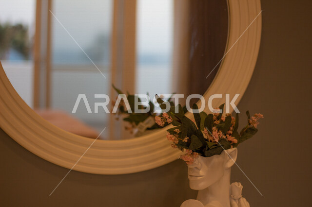 صورة لتحفة بيضاء بها ورد طبيعي و أوراق خضراء بجانب مرايا في غرفة نوم ، تصاميم عصرية و جذابة ، ديكور غرفة نوم رائعة ، تصاميم فخمة و جميلة ، شقق سكنية سياحية ، أوتيل ،  فنادق فاخرة  