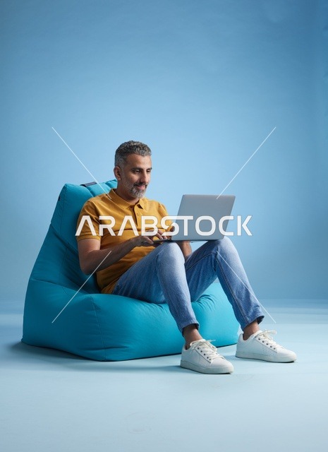 رجل سعودي يعمل على الكمبيوتر المحمول فوق كرسي بين باج