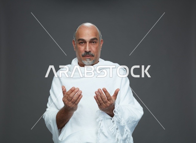 رجل سعودي بملابس الإحرام يدعو على خلفية رمادية