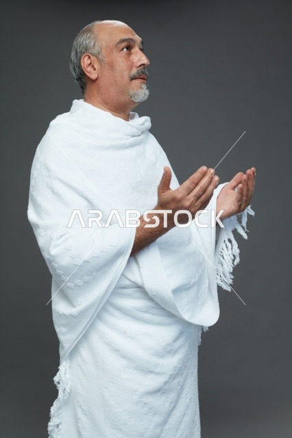 رجل سعودي بملابس الإحرام البيضاء يدعو بخلفية رمادية