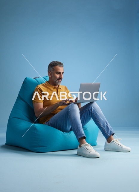 رجل سعودي يعمل على اللابتوب أثناء جلوسه على كرسي بين باق