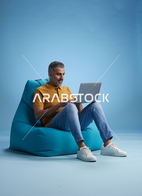 رجل سعودي يعمل على اللابتوب على كرسي بين باق