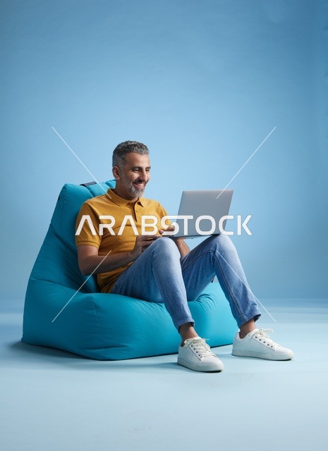 رجل سعودي يعمل على اللابتوب جالسا على كرسي بين باج