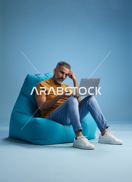 رجل سعودي يعمل على اللابتوب جالساً على كرسي بين باق