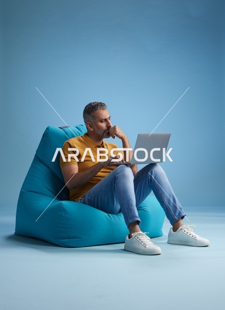 رجل سعودي يعمل على لابتوب أثناء جلوسه على كرسي بين باق