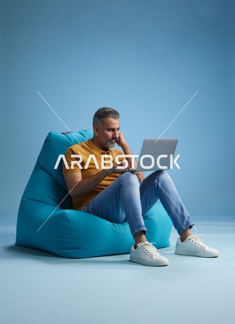 رجل سعودي يعمل على اللابتوب أثناء الجلوس في كرسي بين باج