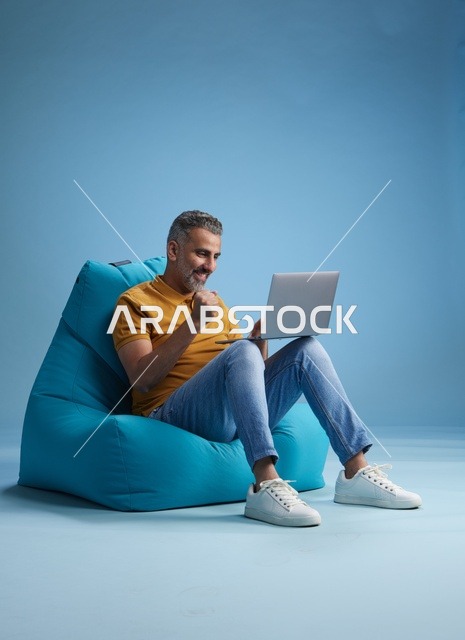 Saudi Man Working on Laptop on Blue Bean Bag