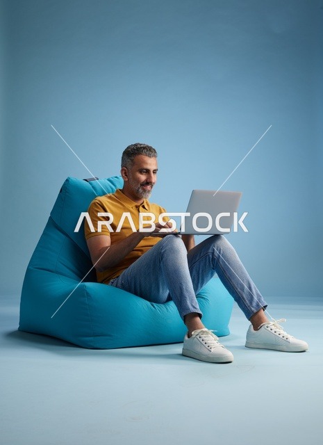 رجل سعودي يعمل على اللابتوب جالساً على كرسي بين باق