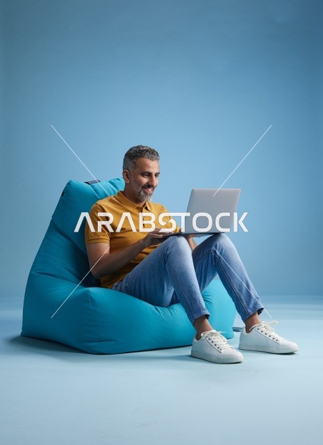 رجل سعودي يعمل على اللابتوب فوق كرسي بين باق