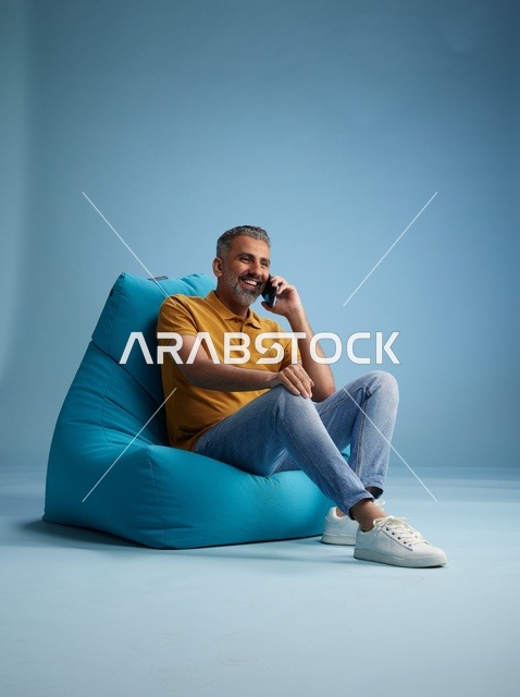 رجل سعودي يتحدث بالهاتف على كرسي بين باق أزرق