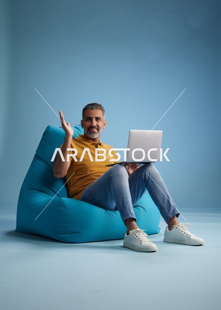 رجل سعودي يعمل على اللابتوب على كرسي بين باق