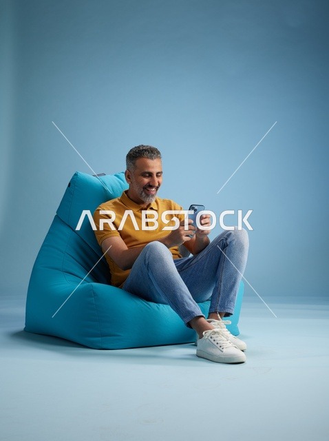 رجل سعودي يستخدم الهاتف الذكي على كرسي بين باق