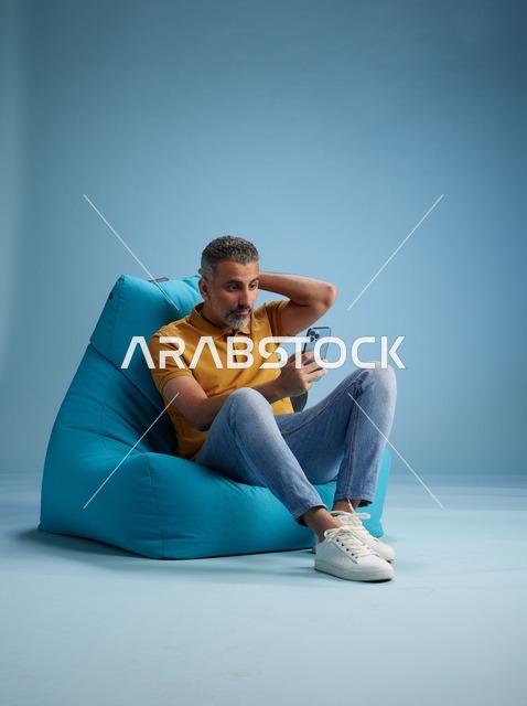 رجل سعودي يستخدم الهاتف الذكي على كرسي بين باق