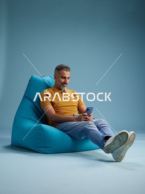 رجل سعودي يستخدم الهاتف الذكي على كرسي بين باق