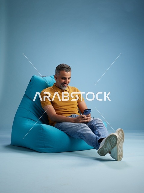 رجل سعودي يستخدم الهاتف الذكي على كرسي بين باق