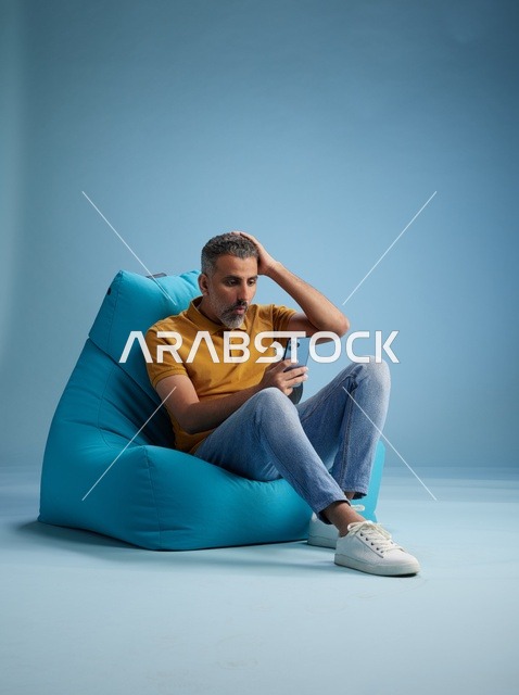 رجل سعودي على كرسي بين باق بتعبير متعجب بالجوال