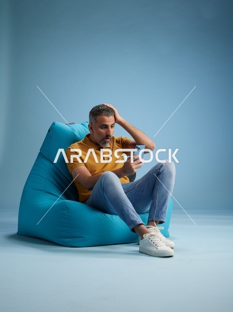 رجل سعودي يستخدم الهاتف الذكي على كرسي بين باق