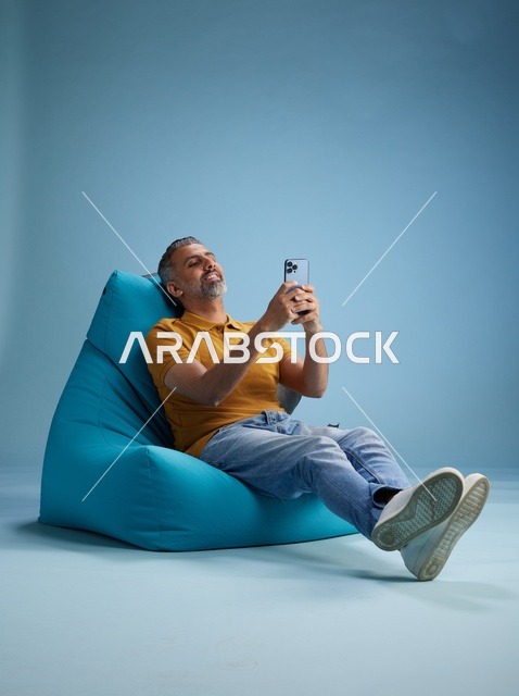 رجل سعودي يستخدم الهاتف الذكي على كرسي بين باق