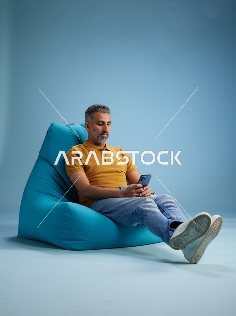 Saudi Man Using Smartphone on Blue Bean Bag Chair