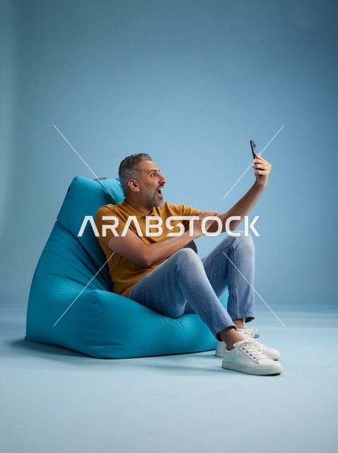 رجل سعودي يلتقط سيلفي على كرسي بين باق في استوديو