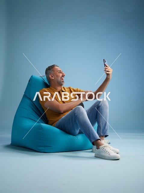رجل سعودي يلتقط سيلفي على كرسي بين باق أزرق