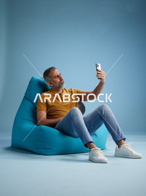 رجل سعودي يلتقط سيلفي جالساً على كرسي بين باج