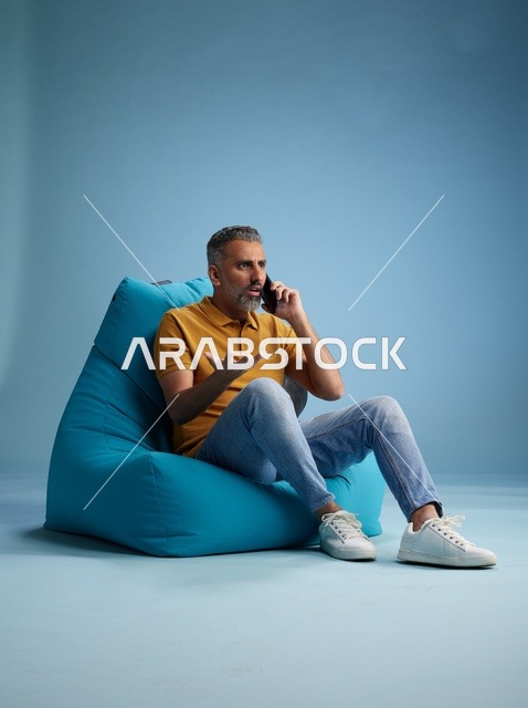 رجل سعودي يتحدث بالهاتف على كرسي بين باق أزرق