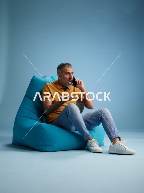 رجل سعودي متفاجئ يتحدث بالهاتف على كرسي بين باج