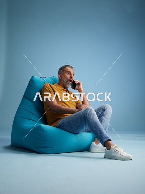 رجل سعودي متفاجئ يتحدث بالهاتف على كرسي بين باق