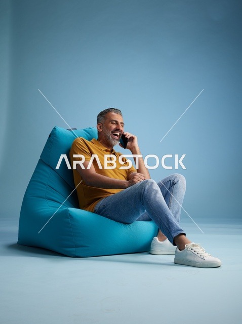 رجل سعودي يتحدث بالهاتف جالساً على كرسي بين باق أزرق