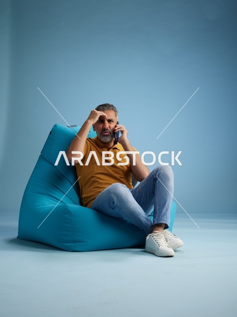 رجل سعودي يتحدث بالهاتف جالس على كرسي بين باج