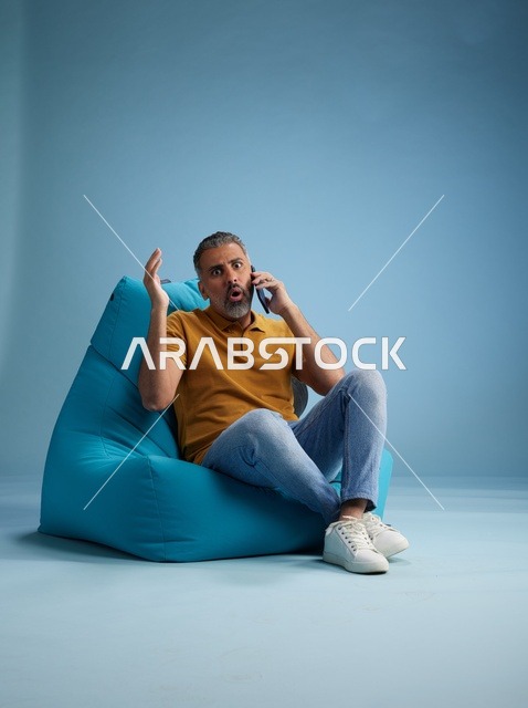 رجل سعودي مندهش يتحدث بالهاتف على كرسي بين باج