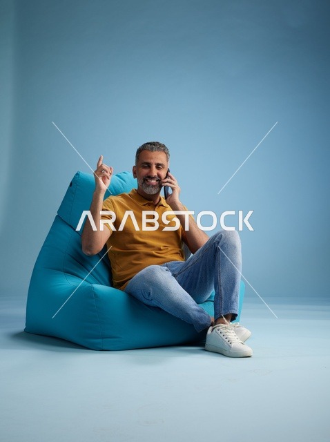 رجل سعودي يتحدث بالهاتف جالساً على كرسي بين باق
