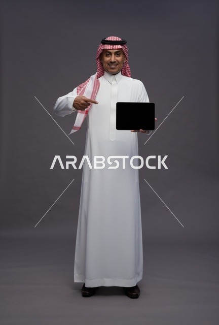 رجل سعودي بالزي التقليدي يمسك بجهاز لوحي