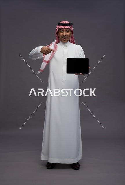 رجل سعودي يشير إلى جهاز لوحي بخلفية رمادية