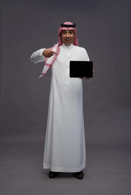 رجل سعودي يشير إلى جهاز لوحي بخلفية رمادية